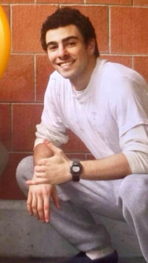 Luigi Mangione in prison garb smiling and looking only as handsome as he can