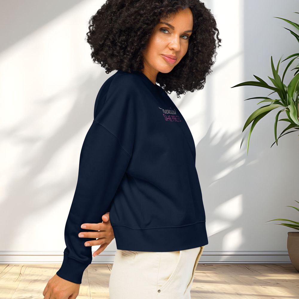 Side view of female model wearing navy crewneck sweatshirt with stylized text graphic that reads "nevertheless she persisted".