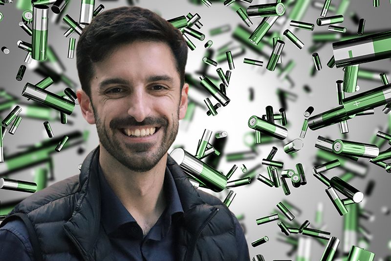 A photograph of a white man with a short dark brown hair and a beard. The background contains a multitude of floating green-colored batteries.