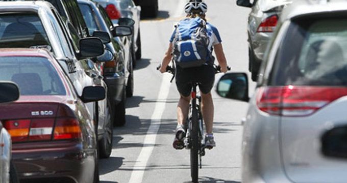 A cyclist wearing a backpack riding between cars