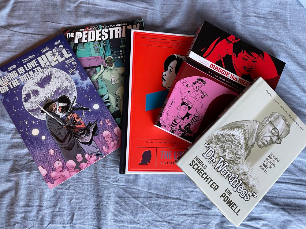 A photo of comics including Falling in Love on the Path to Hell, The Pedestrian, The Love Bunglers, Maggie the Mechanic, and Dr. Werthless