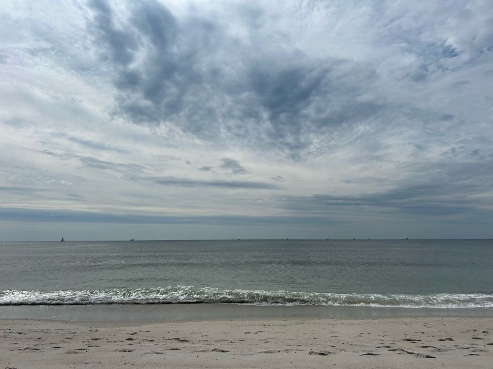Cloudy blue sky over the Atlantic Ocean as a small wave rolls onto the shore