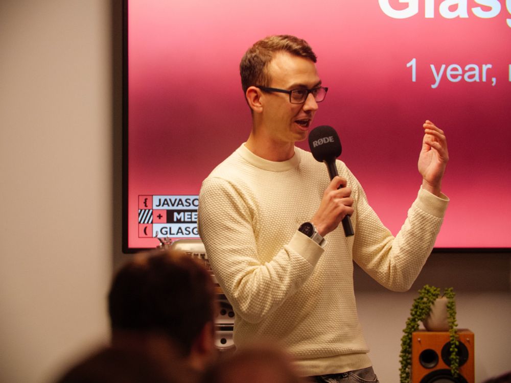 Jamie hosting, standing in front of the GlasgowJs logo and red screen