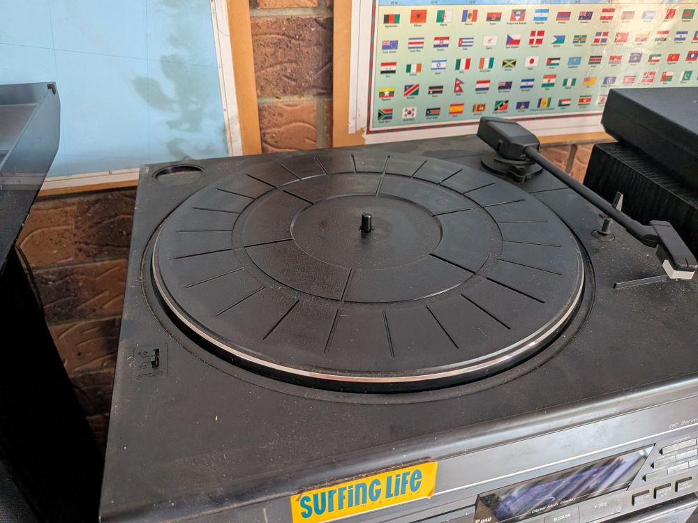 My old record player sitting in its home on top of the rest of my stereo system. The lid is currently off while I reattach one of the hinges.