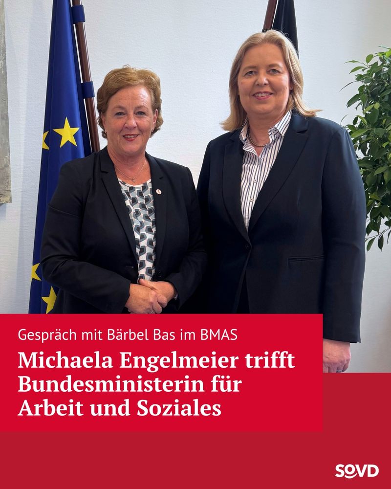 Zwei Frauen stehen nebeneinander und lächeln in die Kamera. Links steht Michaela Engelmeier, die SoVD-Vorstandsvorsitzende, in einem schwarzen Blazer über einer gemusterten Bluse. Sie hält ihre Hände vor dem Körper zusammen. Rechts neben ihr steht Bärbel Bas mit kinnlangem blonden Haar, ebenfalls in einem schwarzen Blazer über einer hellblau-weiß gestreiften Bluse. Beide befinden sich in einem Büro mit heller Wand, hinter ihnen sind zwei Fahnen sichtbar – eine EU-Flagge und eine schwarz-rot-goldene Deutschlandfahne – sowie eine grüne Pflanze. Im unteren Drittel des Bildes befindet sich ein roter Infobalken mit weißer Schrift, der über das Treffen von Michaela Engelmeier mit der Bundesministerin für Arbeit und Soziales berichtet.