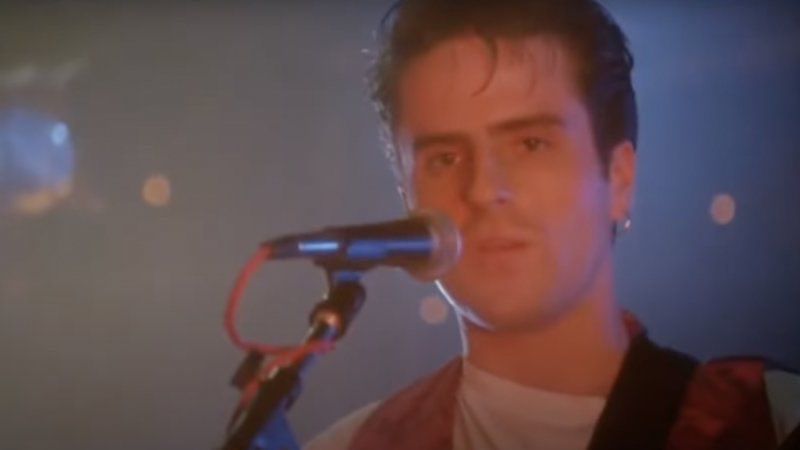 Con O'Neill in Dancin' Thru The Dark. He's standing at a microphone, bathed in pink light.