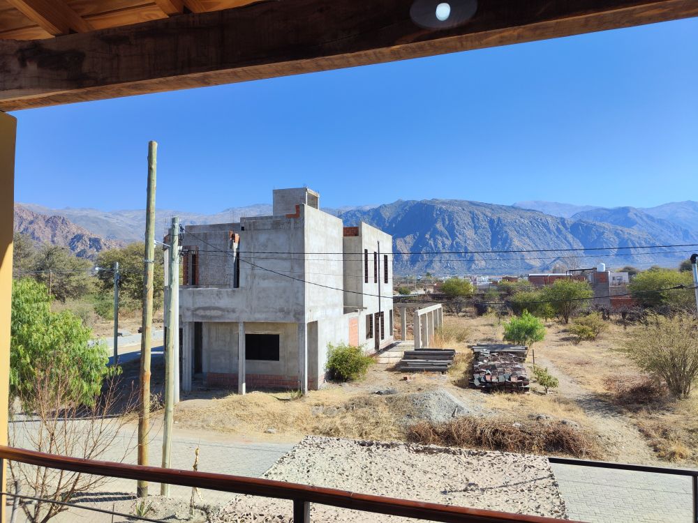 Balcony view from a holiday house showing a house under construction on the opposite side of the street. The background shows mountains and a blue sky. Cafayate, Salta, Argentina 