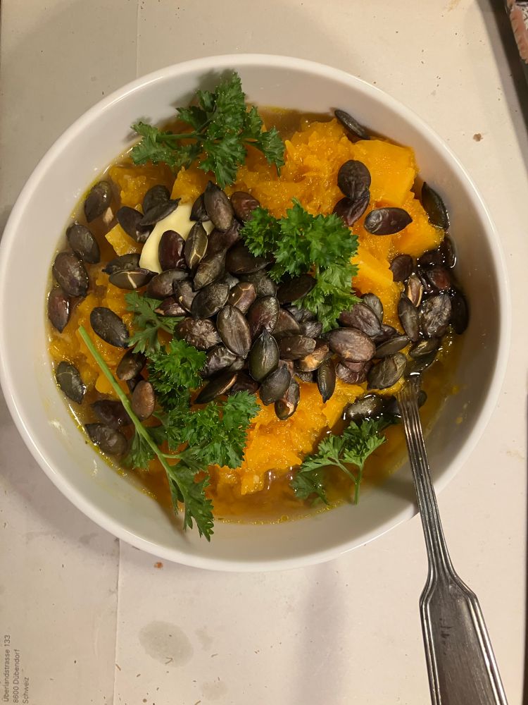 schale mit kürbissuppe garniert mit gerösteten Kürbiskernen, Butter und gekräuselter Pertersilie