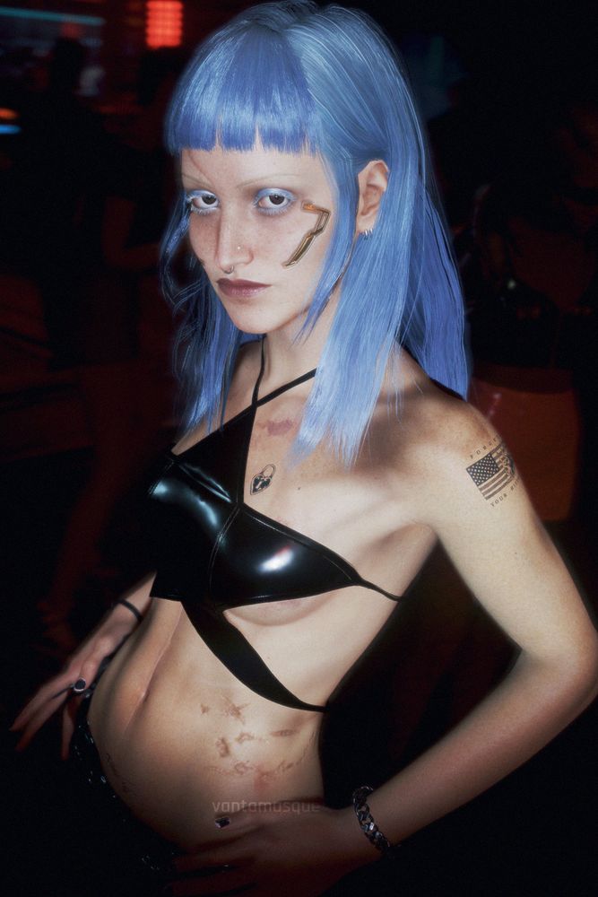 A woman with striking, blunt-bang long blue hair poses in a dark red-lit club environment. Angular gold cyberware marks her cheekbones. She is wearing a shiny black star-shaped leather crop top. She has several visible tattoos, including one resembling a burning American flag on the upper left arm, the words "FORGET YOUR HISTORY" surrounding the flag; another tattoo is a heart-shaped locket over her heart. Her expression is serious, and she is looking directly at the camera. She is illuminated by the camera's flash. Virtual Photography taken in Cyberpunk 2077.