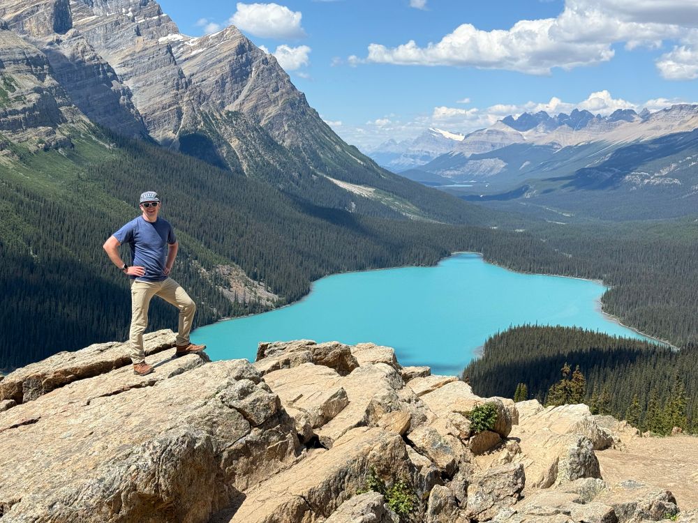 A man in an adventurous pose on a rock overlooking Peyto Lake. 