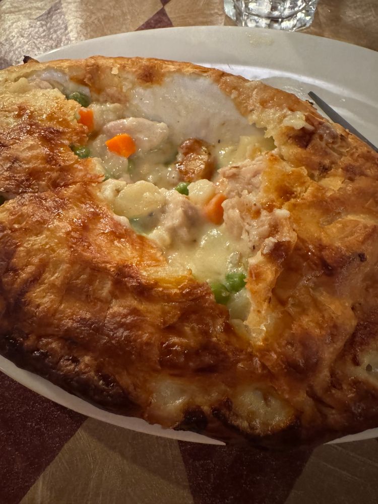 A large turkey pot pie. The crust on top has been broken into so you can see the meet and vegetables inside.