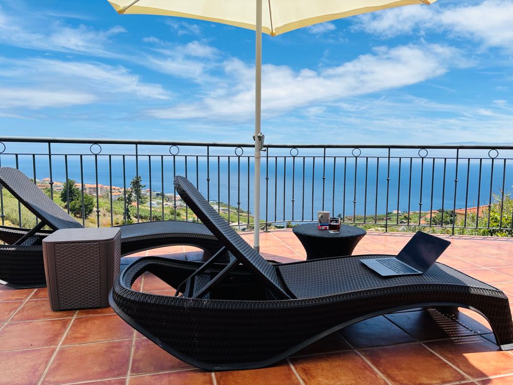 Terassenmöbel unter Sonnenschirm, im Hintergrund der Atlantik vor Madeira. 