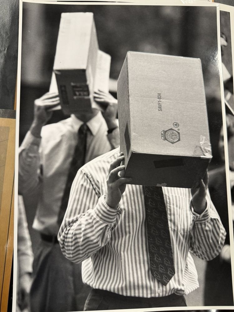 Two men with white shirts and ties hold boxes over their heads to look at the solar eclipse 
