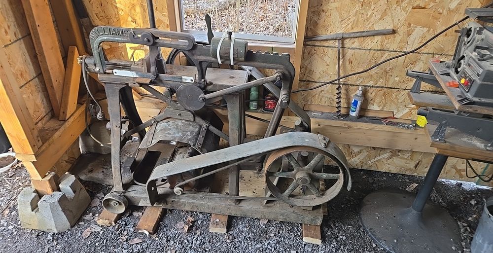 An antique power hack saw in the corner of a modern blacksmith shop.