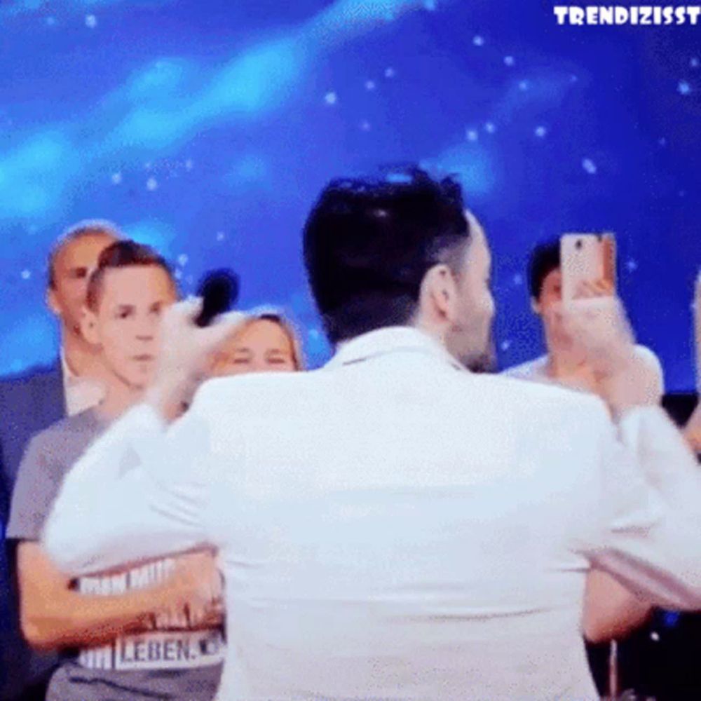 a man in a white suit is taking a picture of himself with a microphone in front of a crowd of people ..