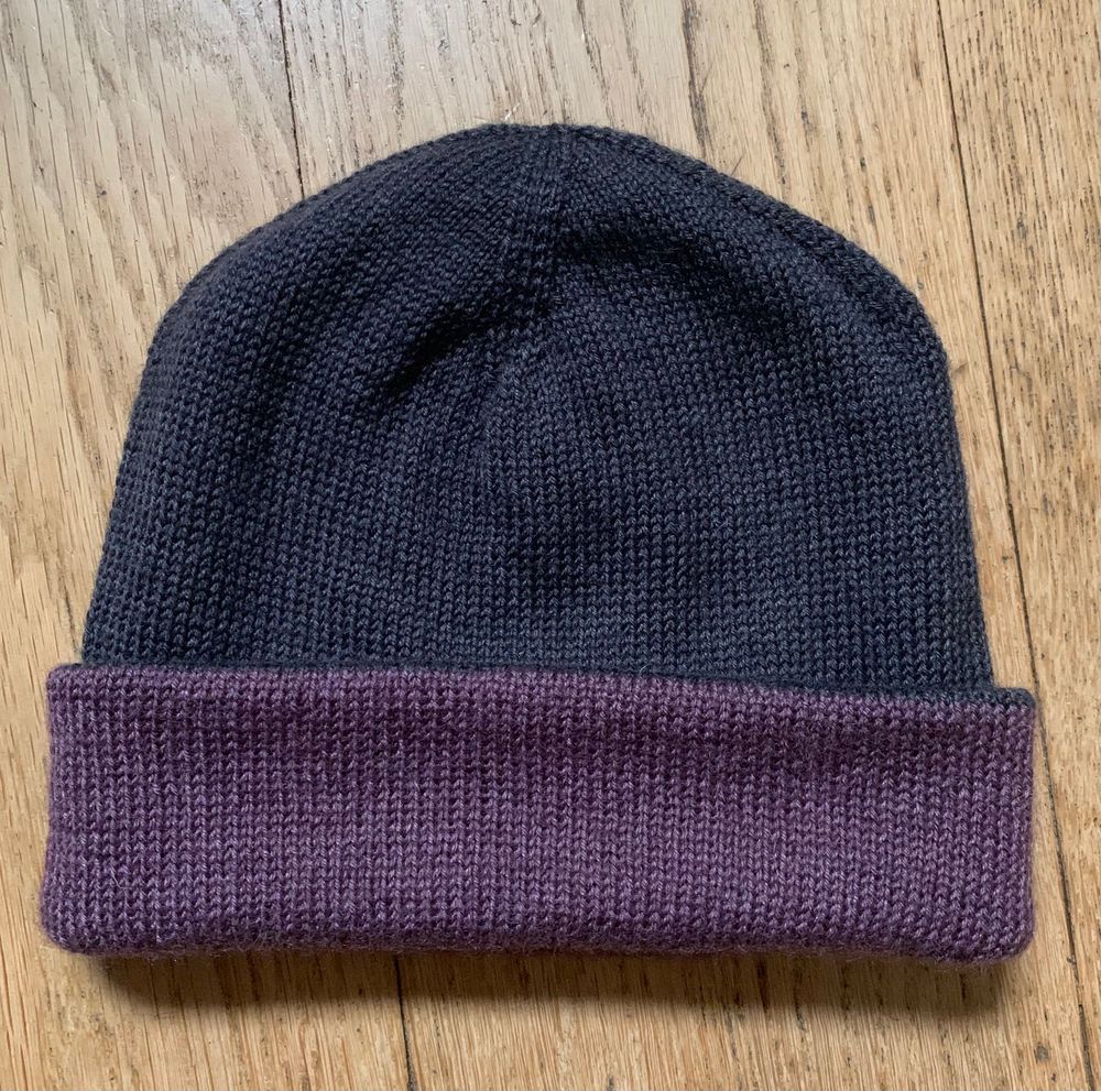 Double layer hand knit hat in stockinette, current folded as black hat with purple brim. 