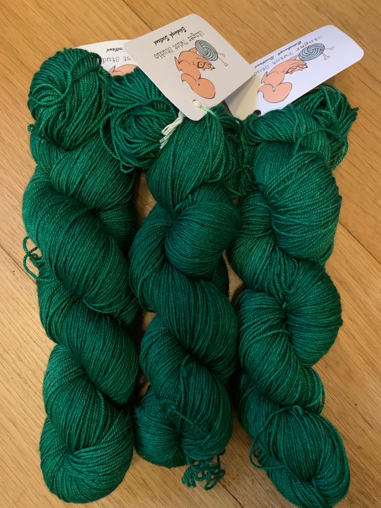 Three unwound skeins of emerald green yarn on a wooden floor. 