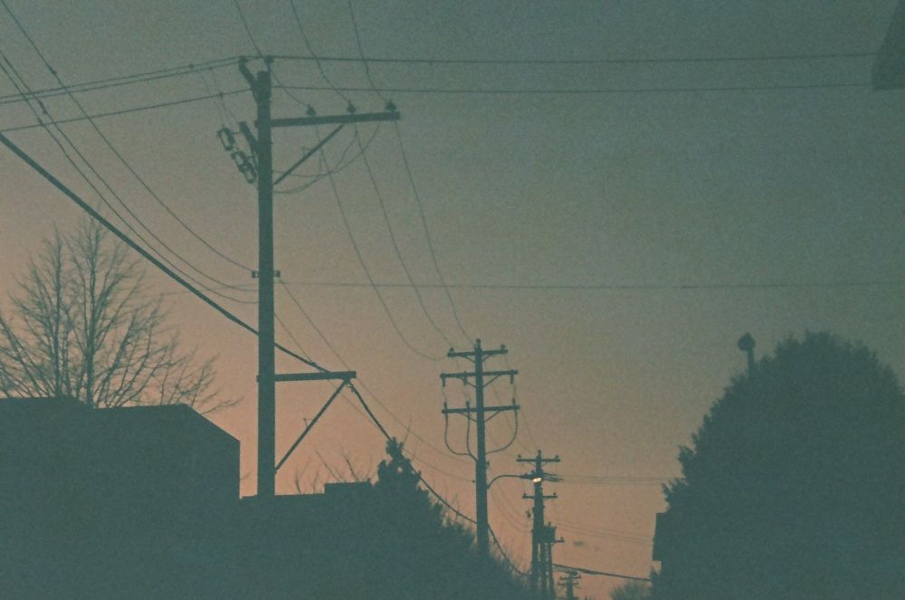 the silhouette of some buildings, trees and electricity posts and wires at sunset 