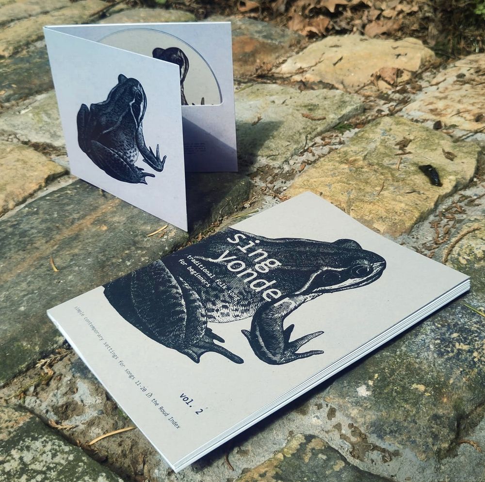 Rather handsome book and CD set of Sing Yonder 2, bearing an illustration of an aloof frog. They are set artistically upon a stone path strewn with dried leaves. It's art, trust me.
