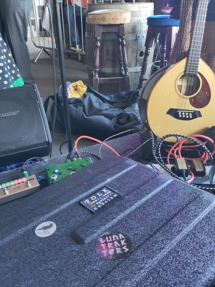 A mandolin on stage. In the foreground an instrument case bears several stickers including the fabulous Folk Against Fascism patch from Lunatraktors. 