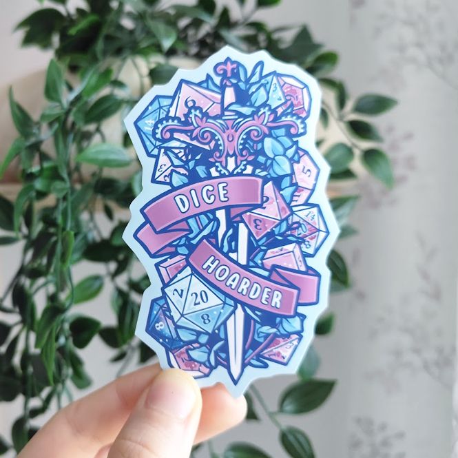 hand holding up a sticker of a sword surrounded by plants and colorful dice, titled "dice hoarder"