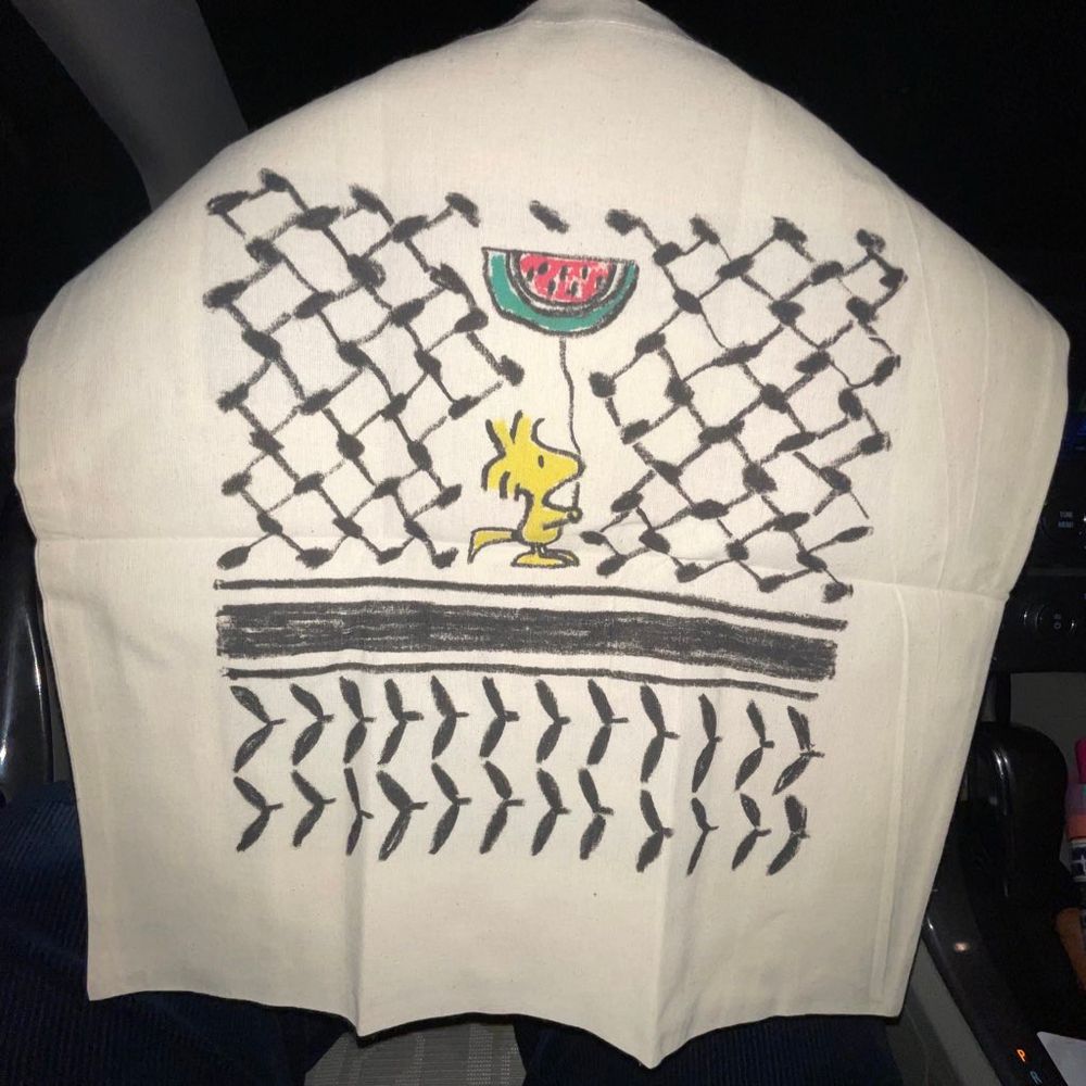 white tote bag with woodstock from peanuts holding a watermelon balloon surrounded by the keffiyeh pattern in black. 