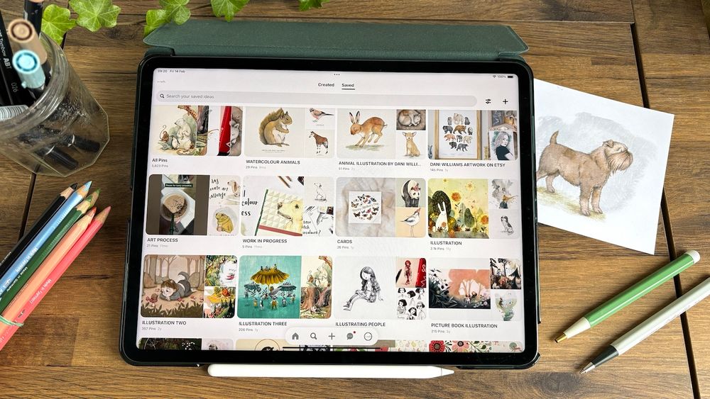 An iPad on a desk. On its screen is a page from Pinterest showing a variety of curated boards about illustration.