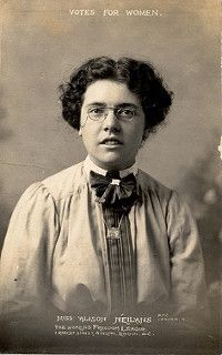 Photographic portrait of Alison Neilans, in Edwardian blouse and neck bow, wearing pince nez, under the text "votes for women".