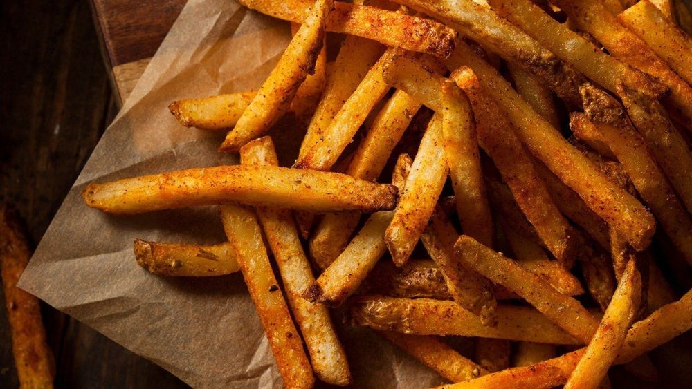 Patatas fritas, crujientes y doradas, sazonadas con especias criollas sobre papel marrón, sazonadas con especias.