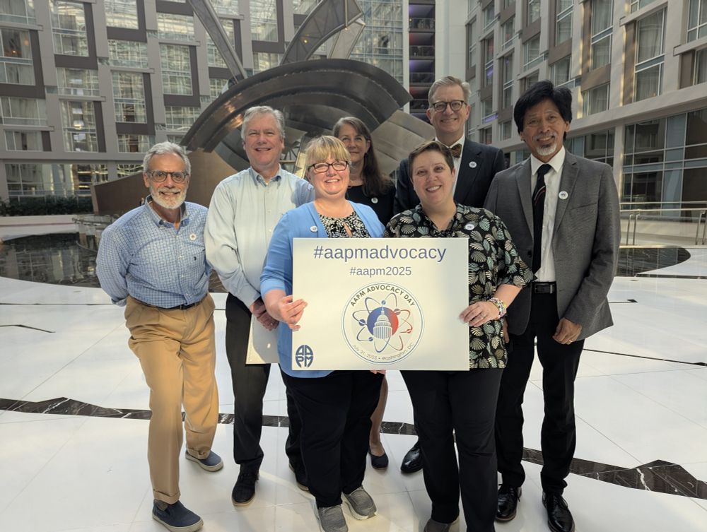 A group of medical physicists standing in a bright atrium, holding a sign for AAPM Advocacy Day