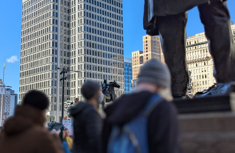 Picture of blurred people in a crowd, with a statue of a person on a horse in the distance. The statue is wearing a green Fletcher Cox Eagles jersey like a cape. Go birds 