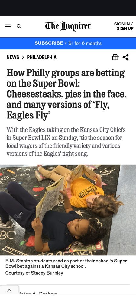 A screenshot of an Inquirer article about Philly  Super Bowl bets, which features a picture of two children laying on a carpet holding books. My kid is looking over at the book her friend is reading. Why read one book when you can read two? Her school is in a reading competition with a school in KC. Go birds