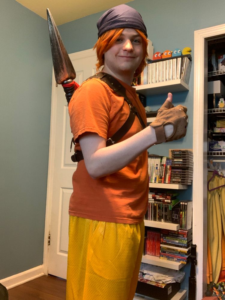 Andrew Ambrose, cosplaying Bandana Dee from Kirby, standing while facing to the side, smiling, and giving a thumbs up