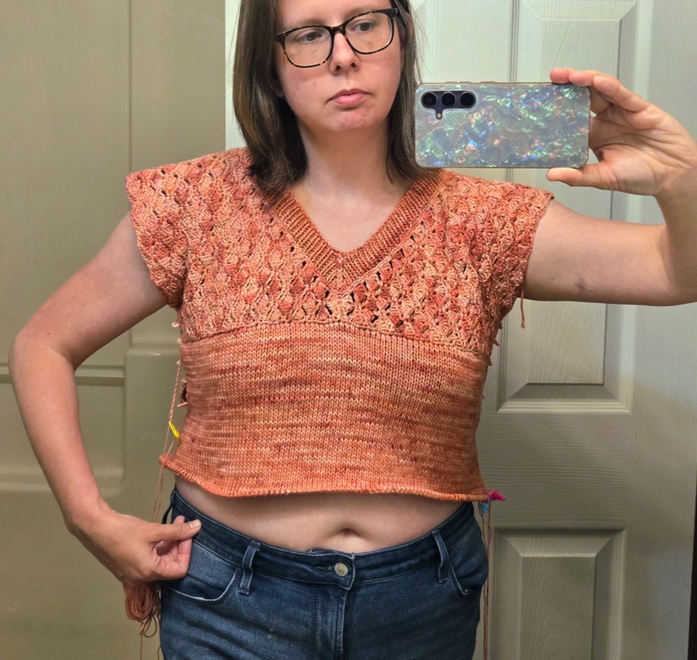 Woman wearing a partially complete crochet and knit top made of blush pink semi solid yarn.