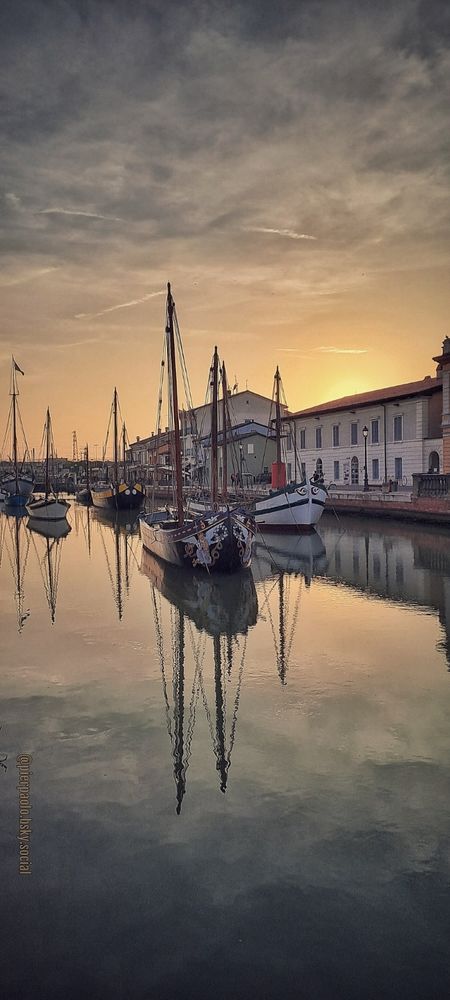 Le imbarcazioni del Museo della Marineria ormeggiate nel Porto Canale  di Cesenatico si riflettono sulle acque al tramonto. In primo piano il "Bragozzo San Nicoló" con due vittorie alate dipinte ai lati della prua, realizzato dal cantiere Schiavon di Chioggia.