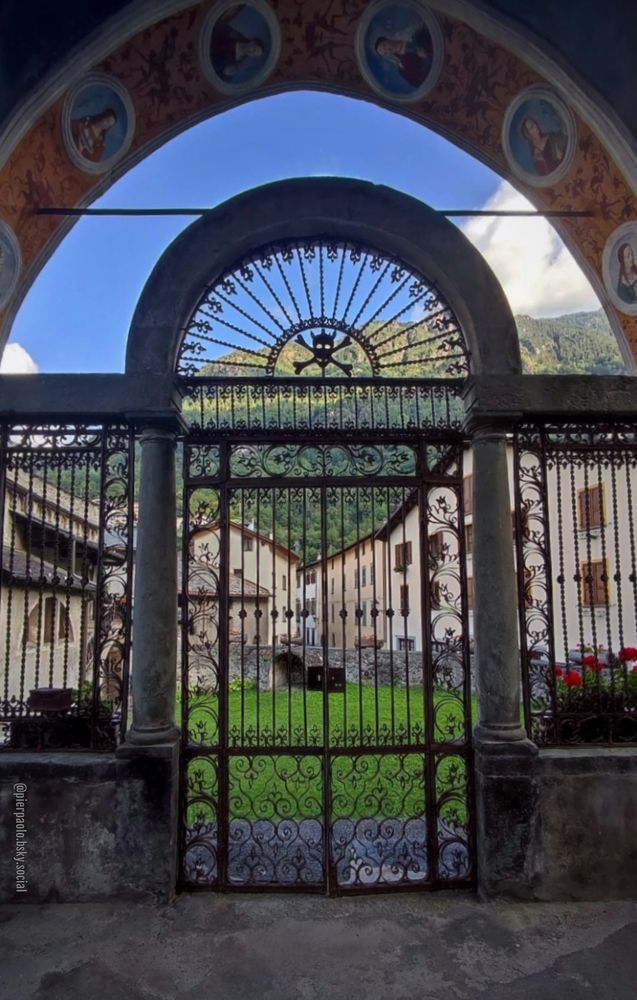 Il cancello di entrata della Cappella Cimiteriale di Grosio (Sondrio) situata accanto alla Chiesa di S. Giorgio (XV secolo). Attraverso il cancello in ferro battuto con, al suo apice, il teschio con le tibie incrociate, si vedono le case del centro abitato di Grosio e le montagne che lo circondano. Nell'arco che sovrasta il cancello, si vedono parte degli affreschi di Cipriano Valorsa (1515 circa-1604). Benché l'antico cimitero non sia più utilizzato, nella cappella sono conservate le spoglie di coloro che morirono durante l'epidemia di peste del XVI secolo.