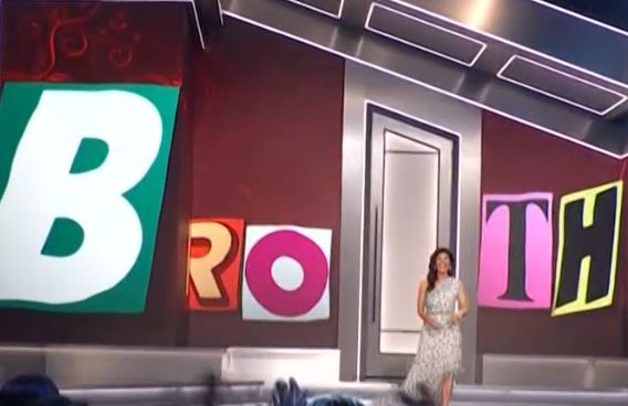 A screenshot of a still from the Bug Brother show. It’s a wide shot where “BROTH” is spelled out in magazine cutout print with Julie presenting.