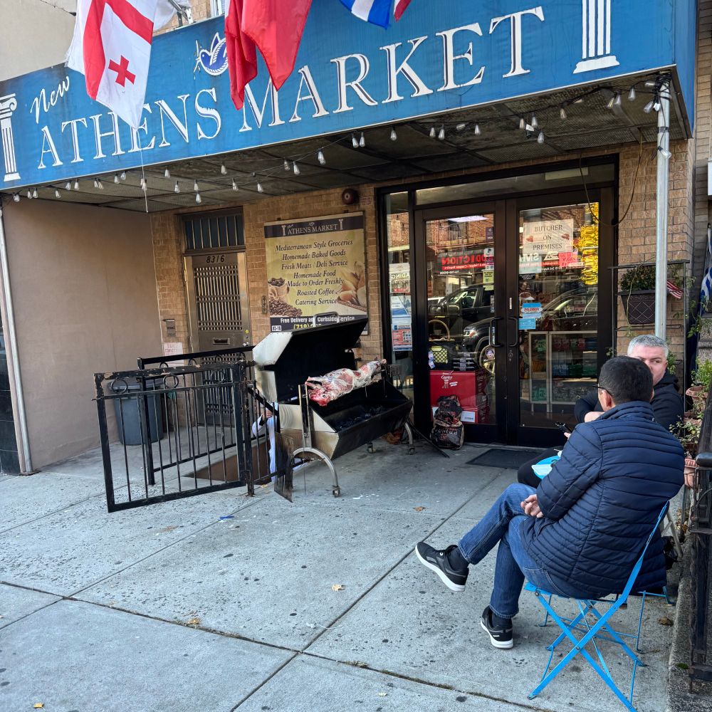 The Athens Market, a Greek convenience store with an animal roasting on a spit while two guys look on in folding chairs