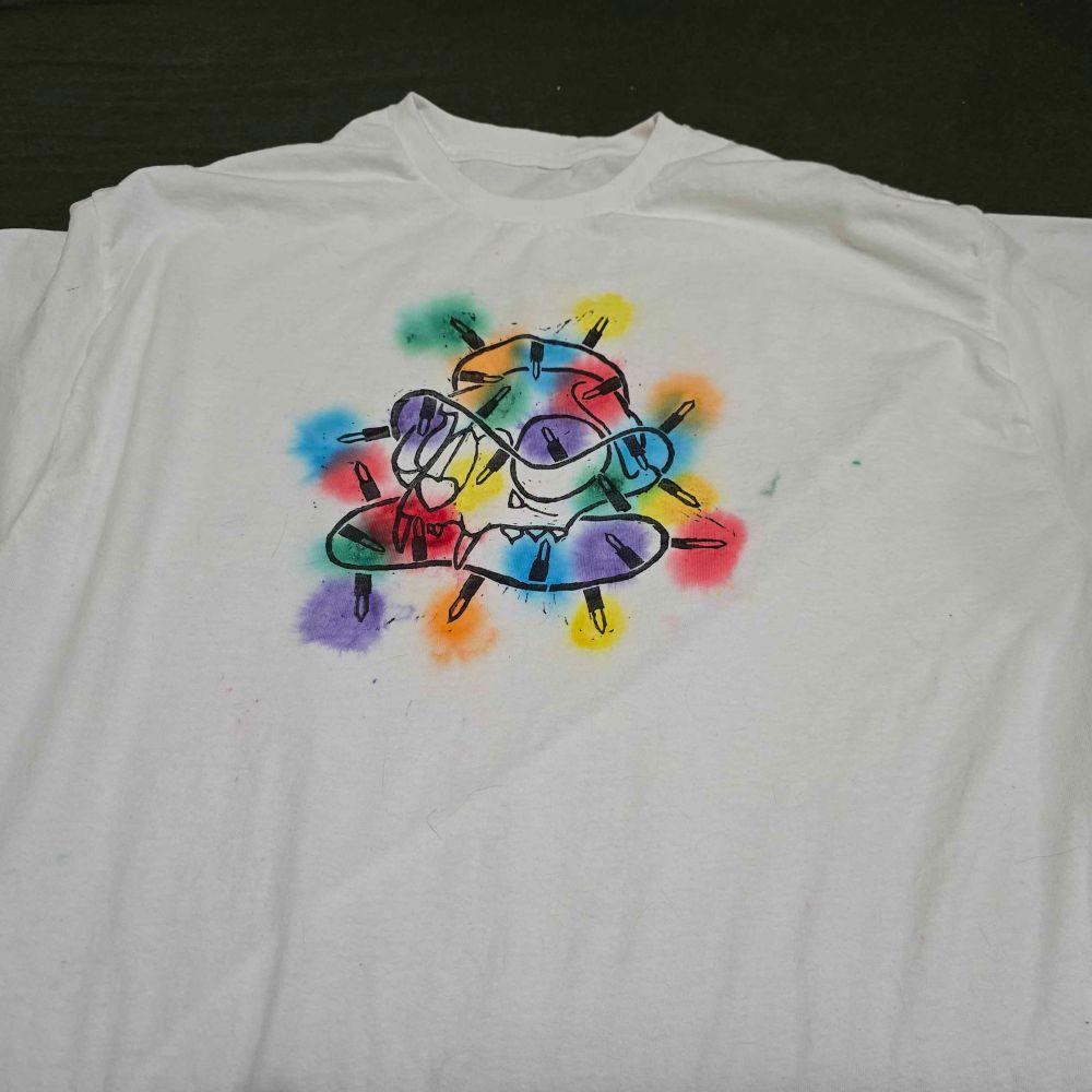 a block print on a white shirt of a cat skull surrounded in Christmas lights that have drops of rainbow dye on them to make it look as if its glowing 
