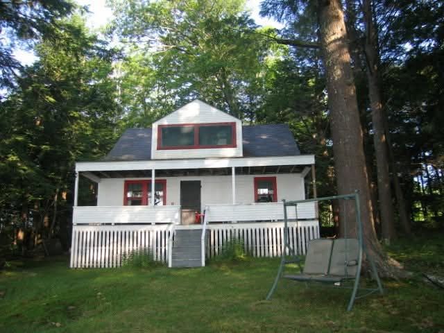 White camp with red trim with big front porch and a swing in the yard