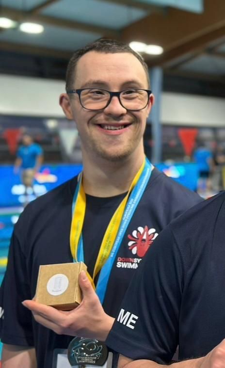Will, a young man, is showing off his medals and smiling broadly.