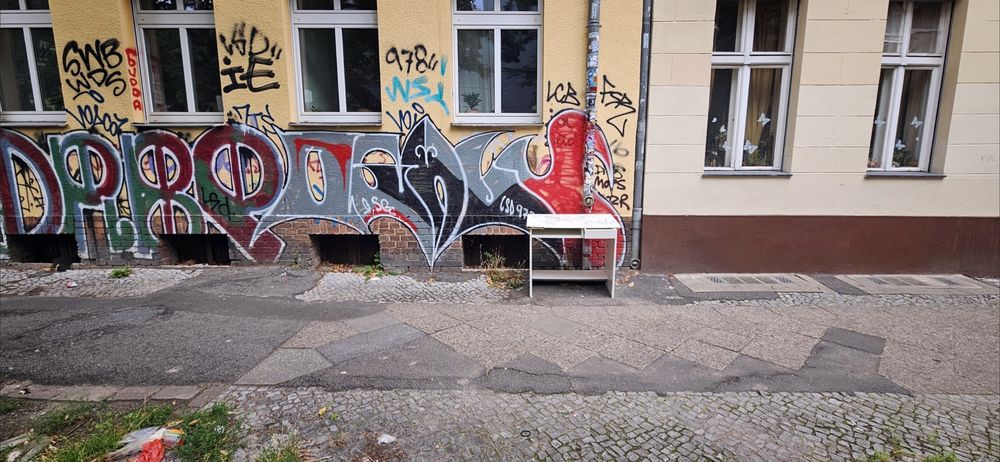 ein kleiner weißer schreibtisch steht vor einer hauswand auf dem gehweg