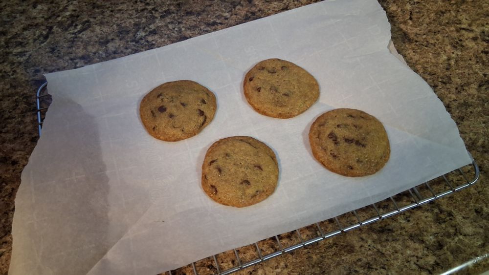 Four freshly baked chocolate chip cookies cooling on a piece of parchment paper.