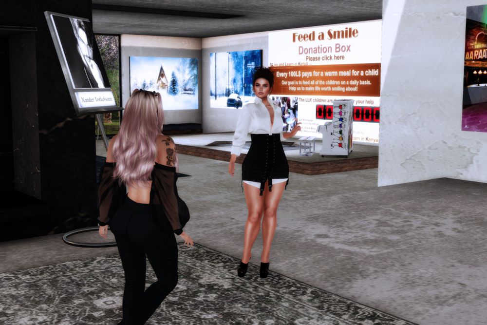 Two women speaking in a gallery with a sign soliciting donations for "Feed a Smile" in the background.
