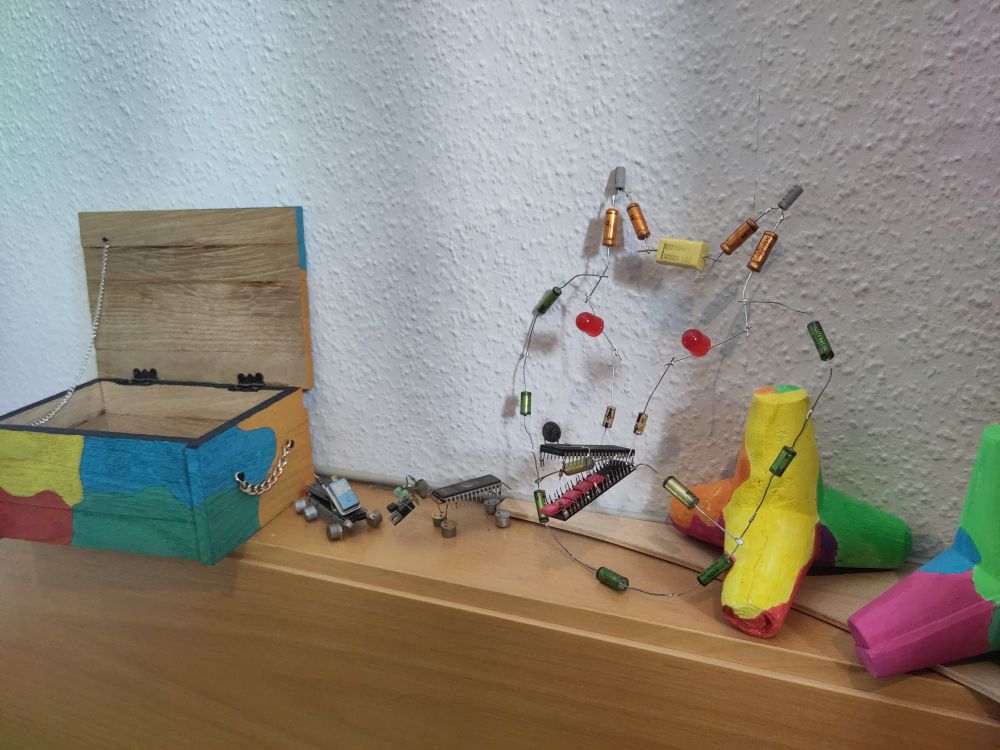 Der stilisierte Wolfskopf im Detail: rote LEDs als Augen, zwei lange ICs als Gebiss, Kondensatoren als Gesicht und Ohren. Kiste, Hund, zwei Tetrapoden und LKW auch zu sehen