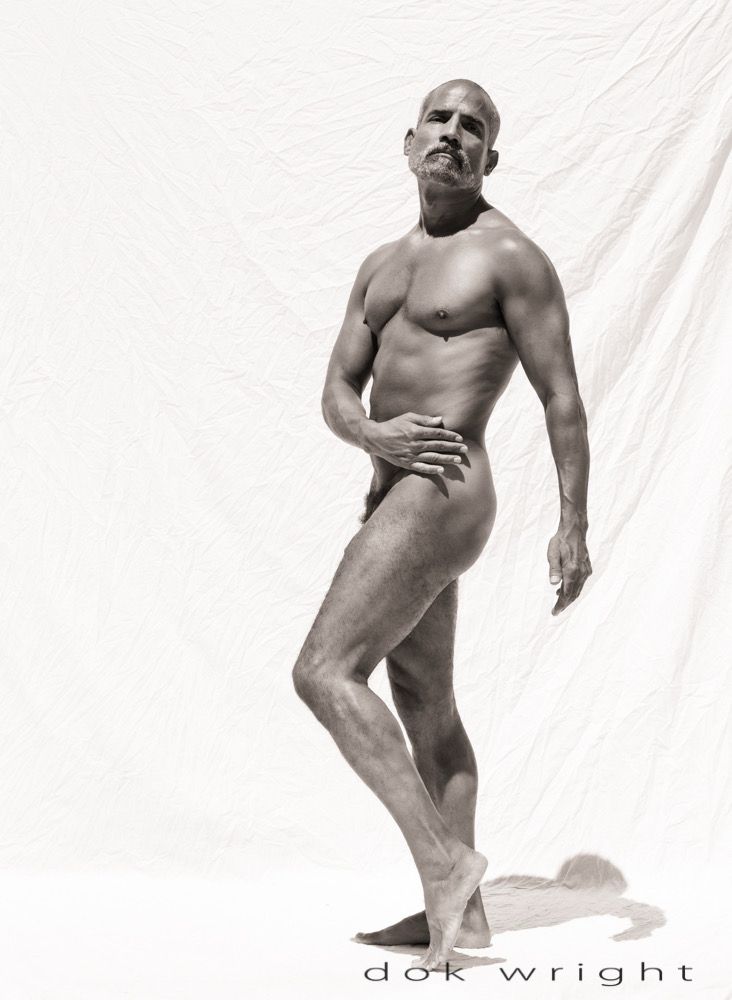 Male figure on white background. He is standing in a slight twist, right hand across his body on his hip and the left hand dangling down. His left leg is bent at the knee slightly. 