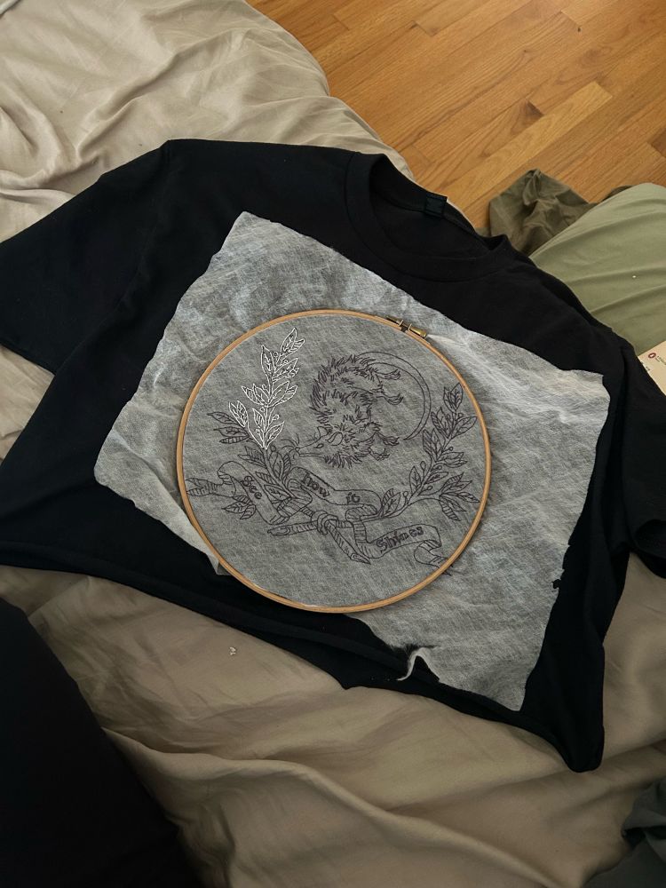 Black crop top with an unfinished design of an oppossum in a laurel wreath with the Hozier song lyrics “see how it shines” written on a ribbon.  