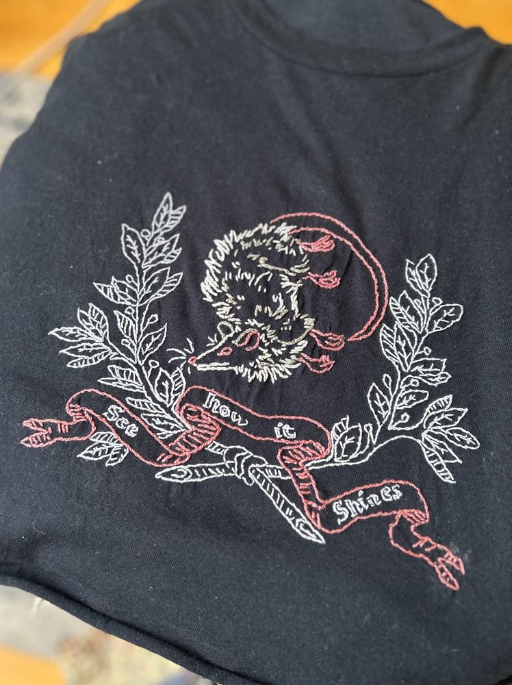 Finished design on back crop top with a white, gray, and pink oppossum in a white laurel wreath with the Hozier song lyrics “see how it shines” written on a pink ribbon.  