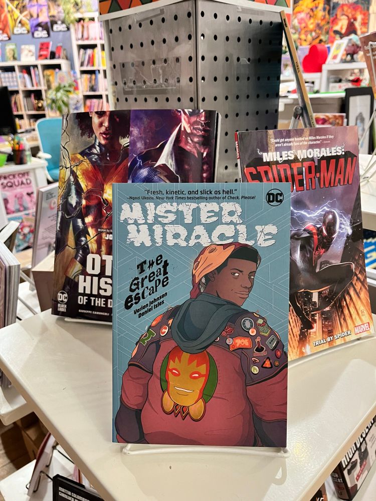 A bookstore shelf displays Mister Miracle: The Great Escape, The Other History of the DC Universe, and Miles Morales: Spider-Man: Trial by Spider