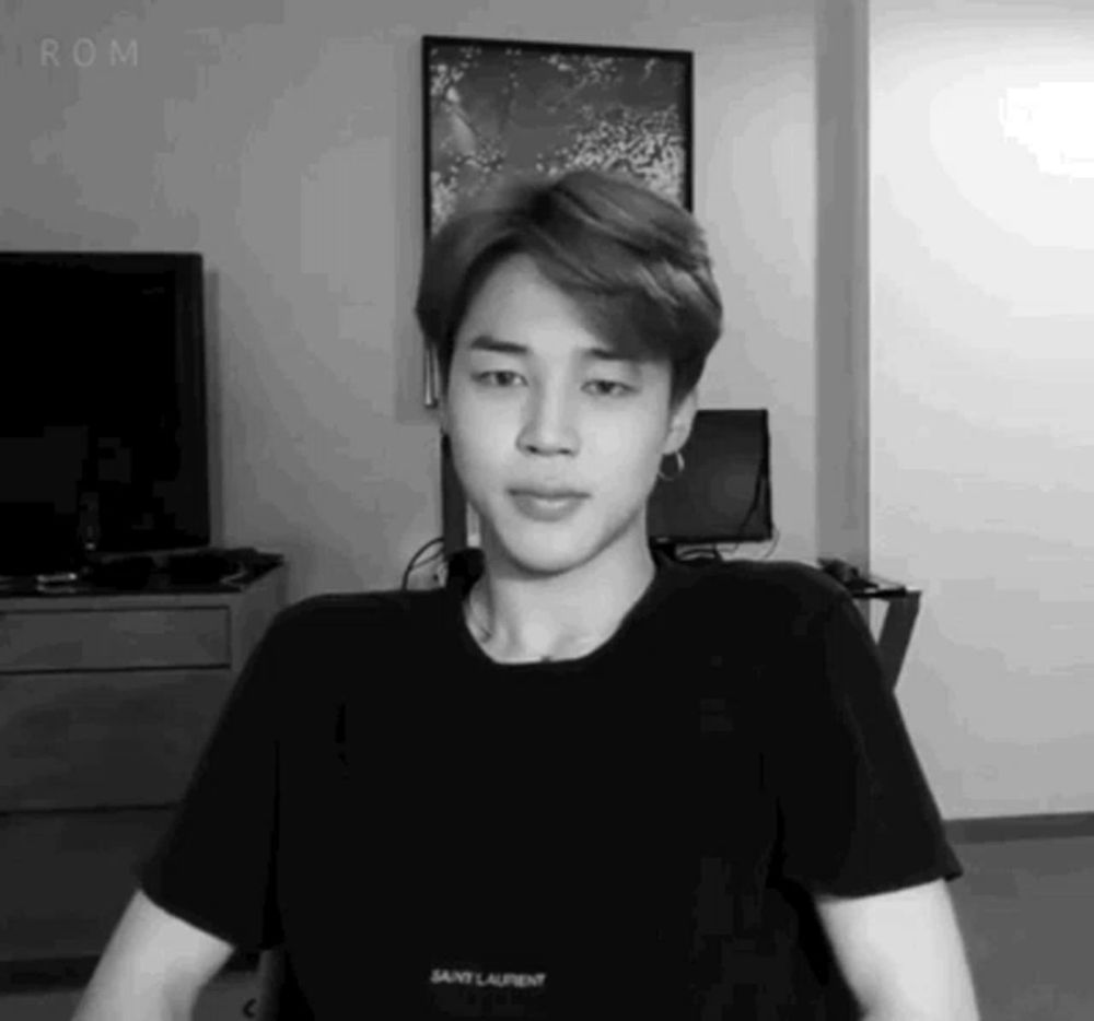 a black and white photo of a young man wearing a black t-shirt and earrings .